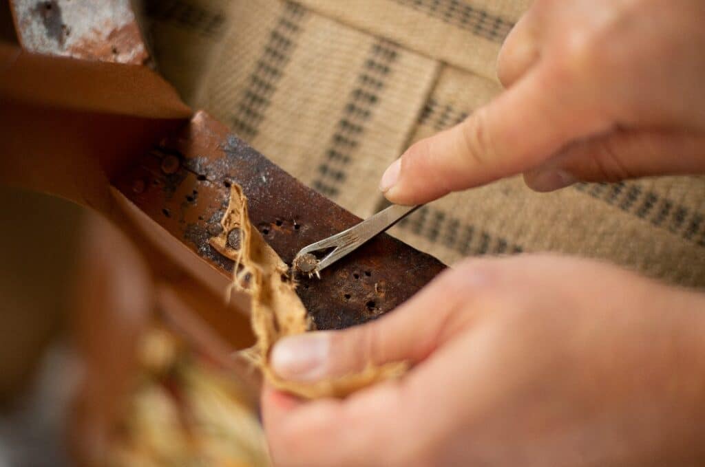 A close up of upholsterer's hands removing antique upholstery nails. Restoration of an antique chair.